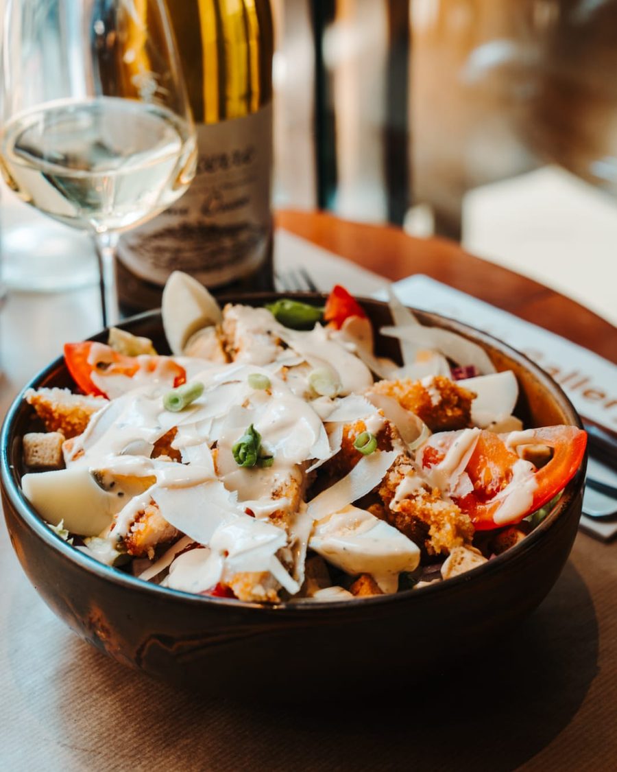 Salade Caesar du Café Gallery : poulet pané, copeaux de parmesan, œuf et tomates, servie avec un verre de vin blanc