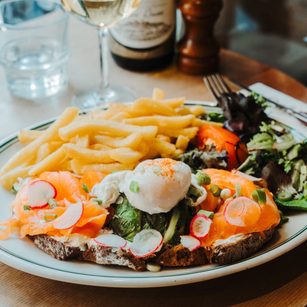 Tartine de saumon fumé et avocat surmontée d'un œuf poché, servie avec frites maison et salade au Café Gallery