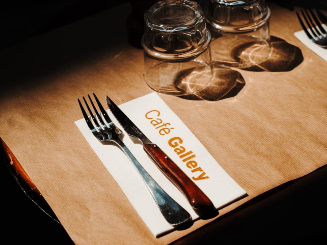 Couvert dressé sur papier kraft au Café Gallery, serviette blanche portant le logo doré de la maison