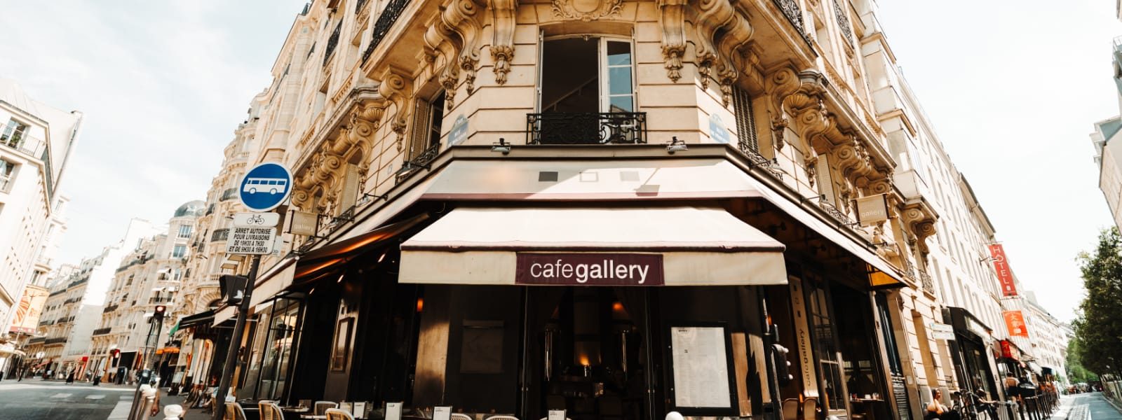 Devanture d'angle du Café Gallery sous son store bordeaux, terrasse en chaises de rotin, immeuble haussmannien rue de Provence à Paris 9e