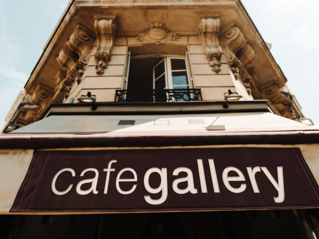 Enseigne blanche « cafegallery » sur store bordeaux, photographiée en contre-plongée devant la façade haussmannienne