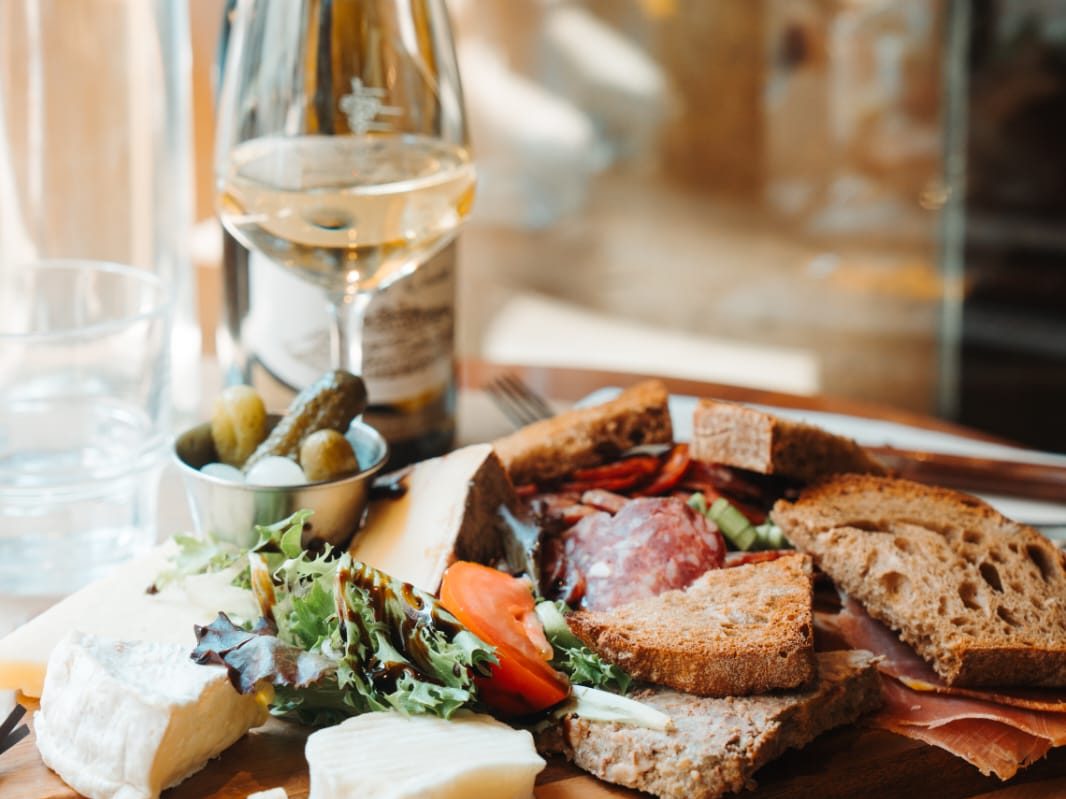 Planche de charcuterie et fromages du Café Gallery : jambon sec, saucisson, brie, cornichons et pain de campagne, avec du vin blanc
