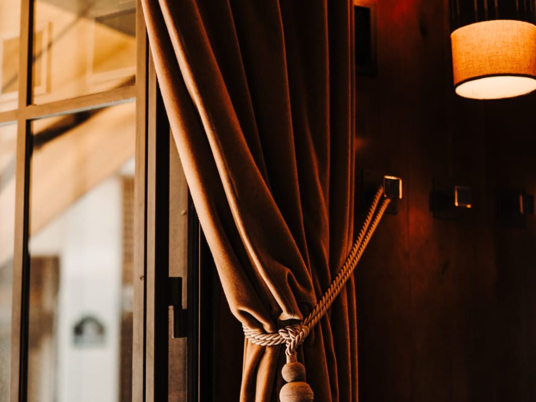 Rideau de velours caramel retenu par une embrasse à pompon, à côté d'une lampe cylindrique du Café Gallery
