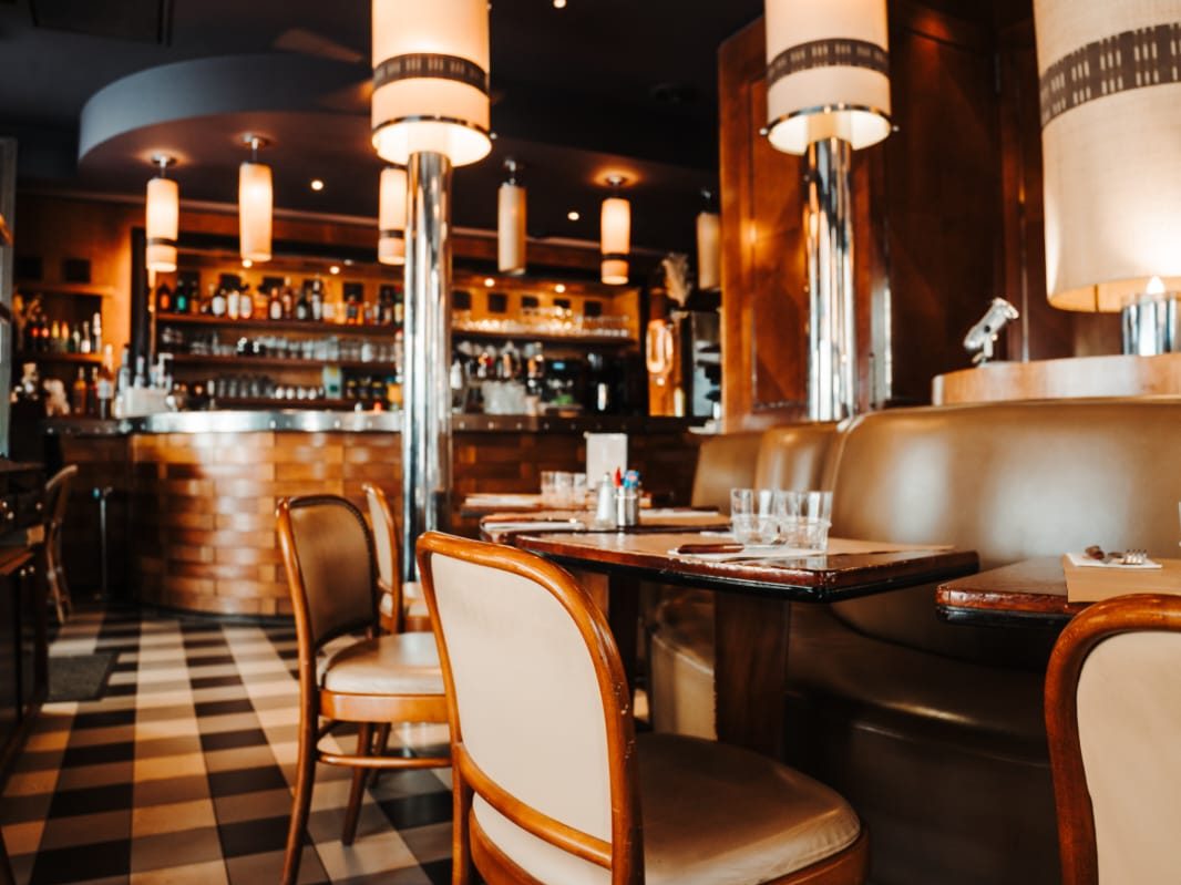 Salle du Café Gallery : banquettes de cuir, chaises bistrot en bois courbé, lampes cylindriques et sol en damier noir et blanc