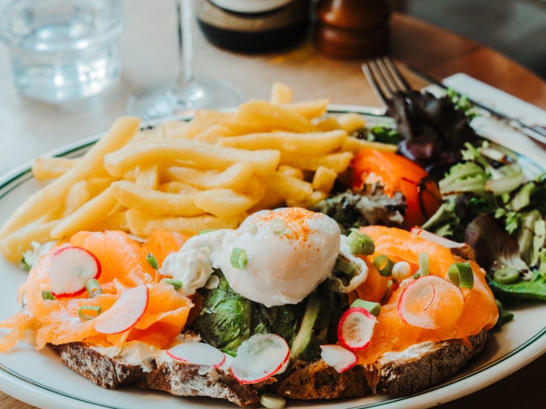 Tartine de saumon fumé et avocat surmontée d'un œuf poché, servie avec frites maison, radis et salade au Café Gallery