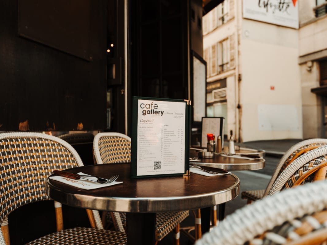Carte de l'apéritif du Café Gallery posée sur une table ronde en zinc, chaises tressées et Galeries Lafayette en arrière-plan